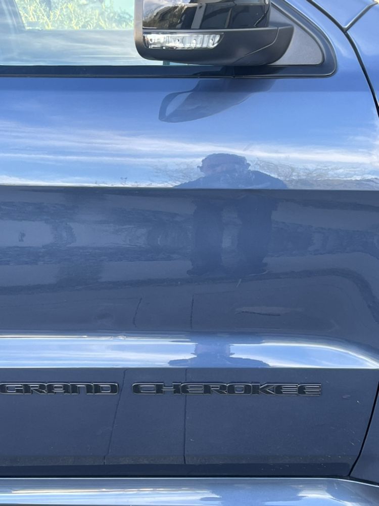 Close-up of a blue Jeep Grand Cherokee's door, side mirror, and black lettering badge.