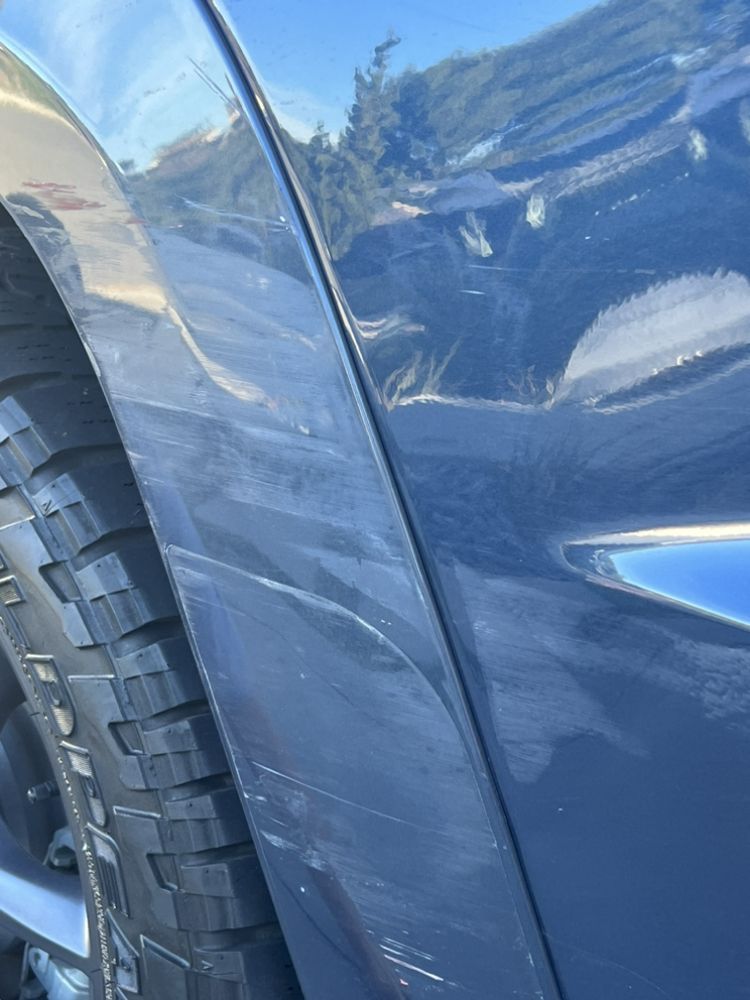Scratched dark blue plastic wheel well trim and fender panel on a car.