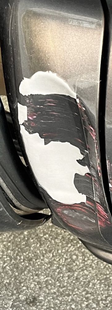 A close-up of a vehicle bumper with a large patch of paint chipped off, revealing a white primer layer.