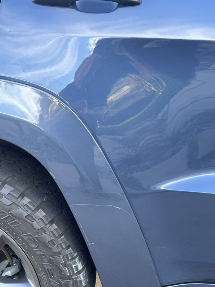 A close-up view of a blue car's rear quarter panel showing light, superficial scratches near the wheel well.