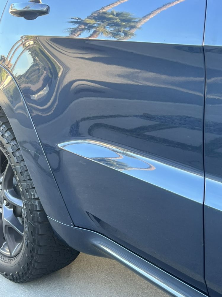 A close-up of a blue car's rear panel and door, showing reflections of palm trees and a bright, sunny outdoor setting.