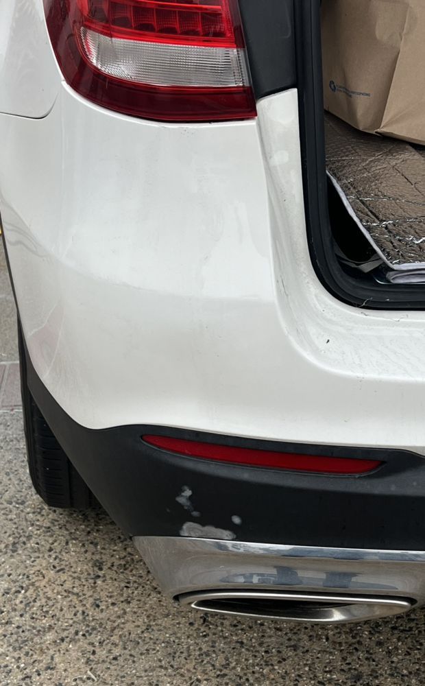 Close-up of a white SUV's rear bumper showing paint chipping on the black plastic trim above the exhaust pipe.