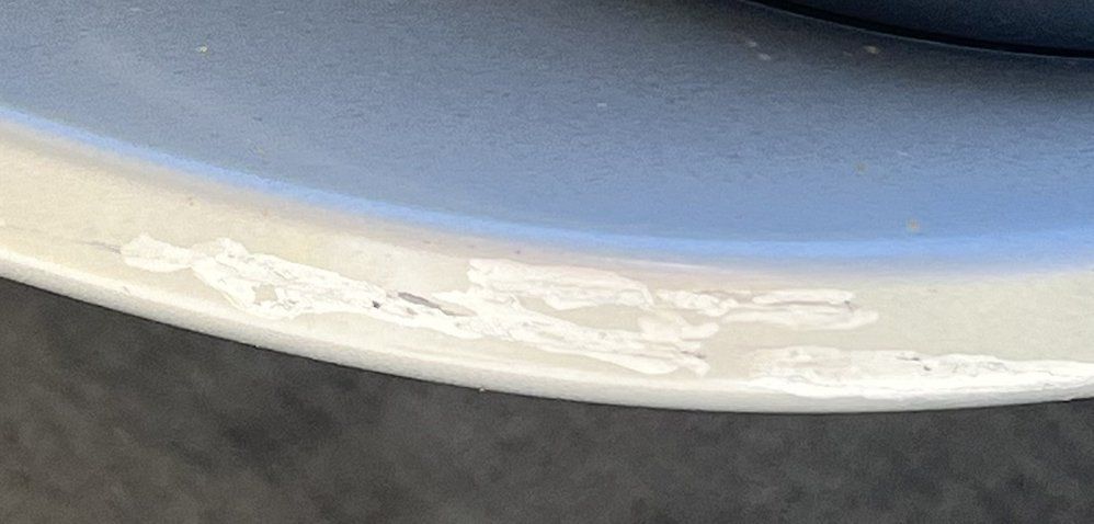 Close-up of a white car bumper showing significant paint scuffs, scratches, and damage along the bottom edge.