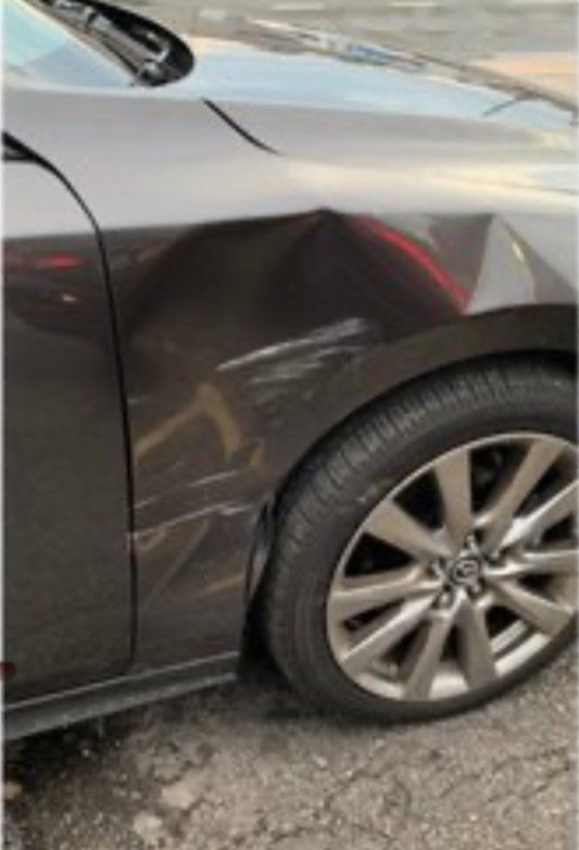 Close-up of a dark brown car's front fender showing a dent and surface scratches above the tire.