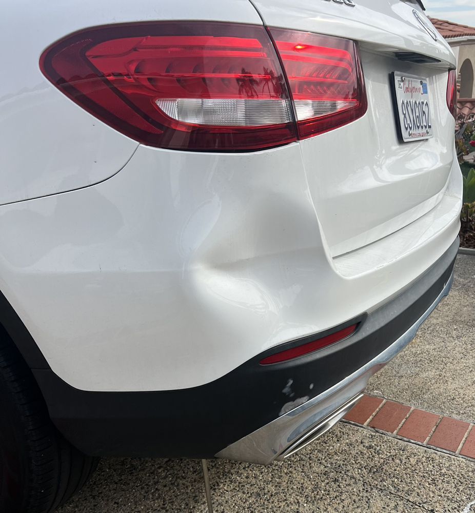 A close-up of a dent on the white rear bumper and quarter panel of a Mercedes-Benz SUV.