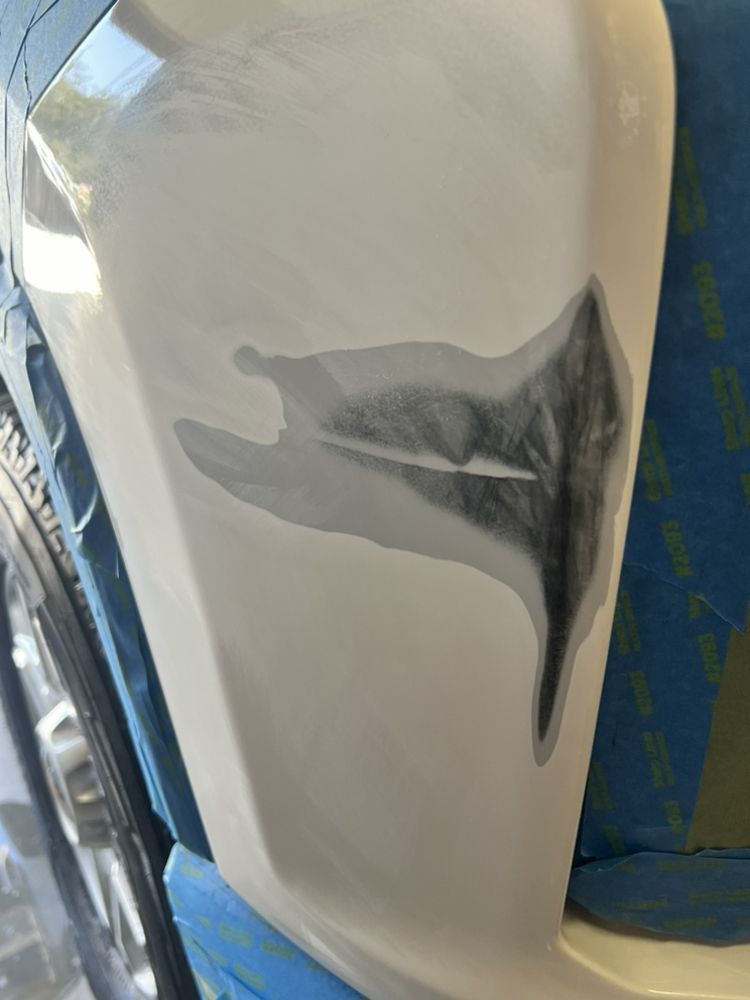 Close-up of a white car bumper showing a sanded area with a deep scratch prepared for auto body repair.