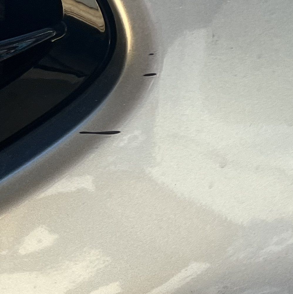 Close-up of three small, dark scratches on the light-colored car paint near the window trim.