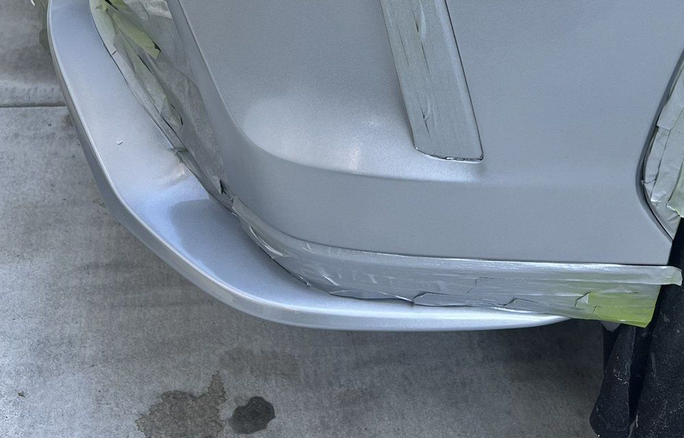 A close-up view of the front bumper of a gray car undergoing repair, showing taped seams and a smoothed surface.