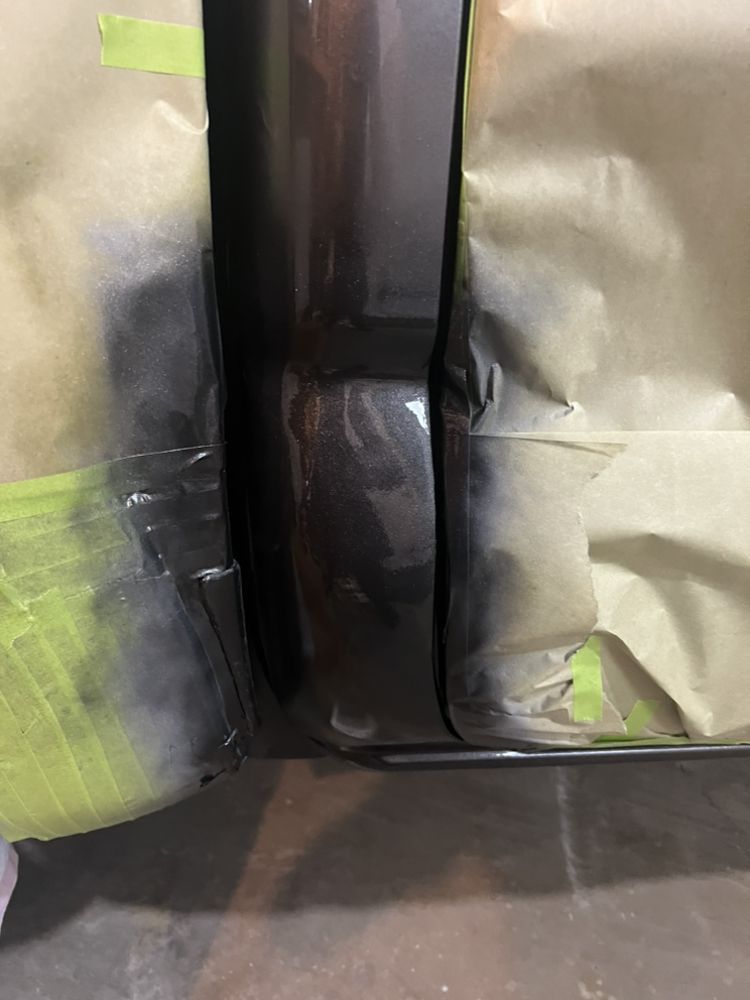 A car door panel and frame masked with tape and brown paper, prepared for automotive paint work.