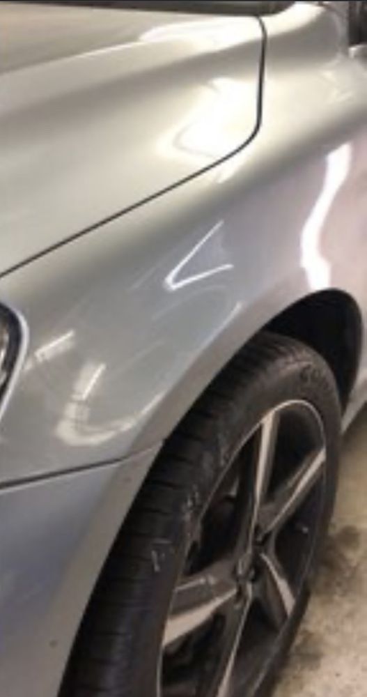 A close-up of a silver car's front fender and wheel in a garage.