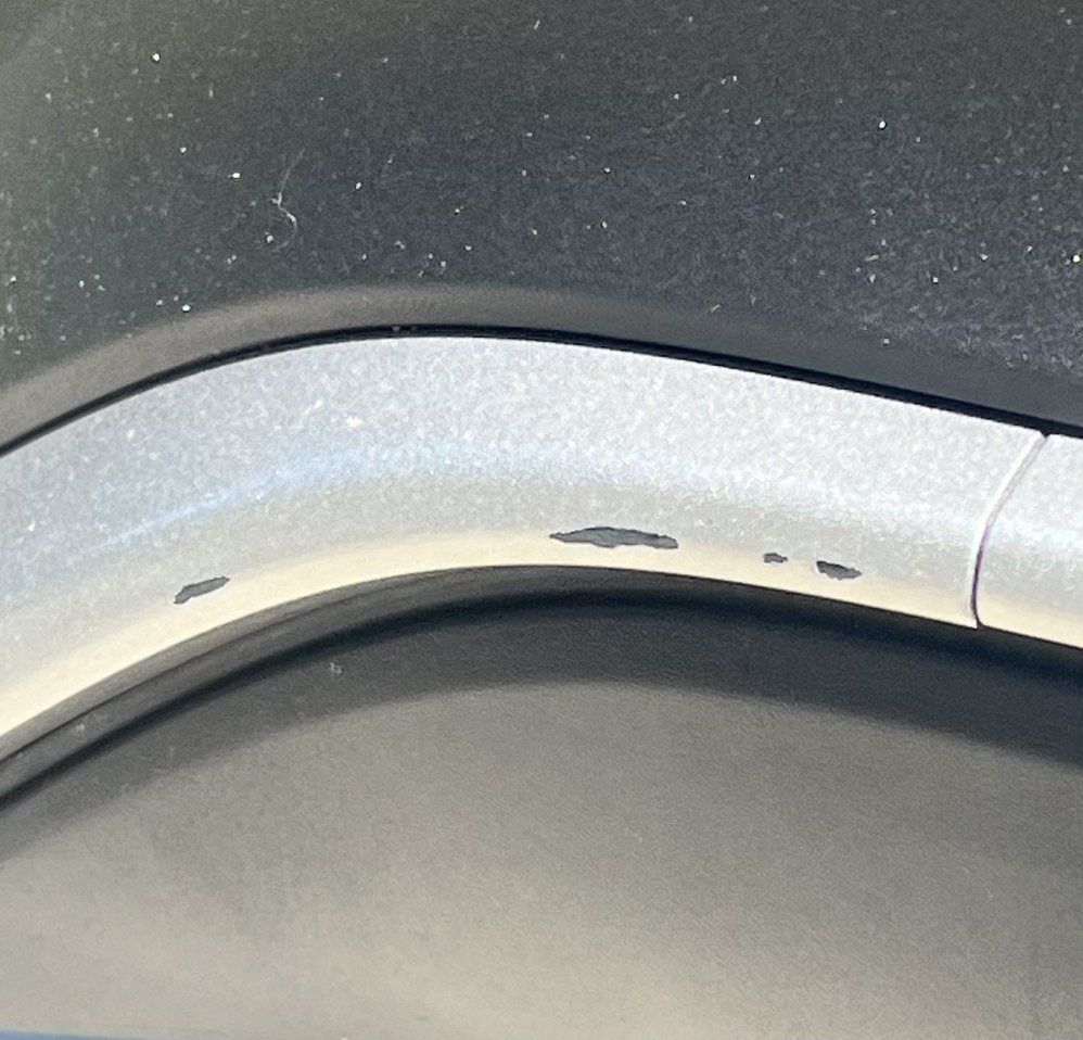 A close-up view of silver-painted wheel arch trim with several small paint chips showing the dark material underneath.