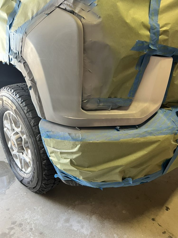 A vehicle fender and bumper masked with tape and paper in preparation for automotive bodywork or paint.
