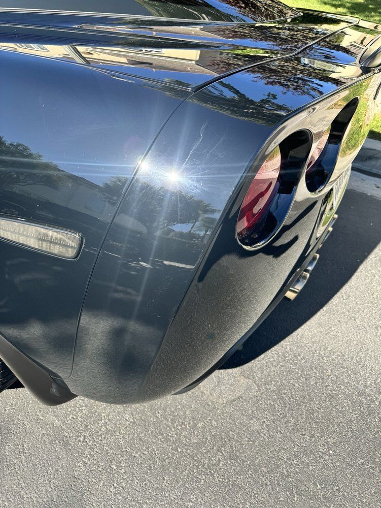A close-up view of the rear corner of a dark-colored Chevrolet Corvette, showing the taillight and body panel lines.