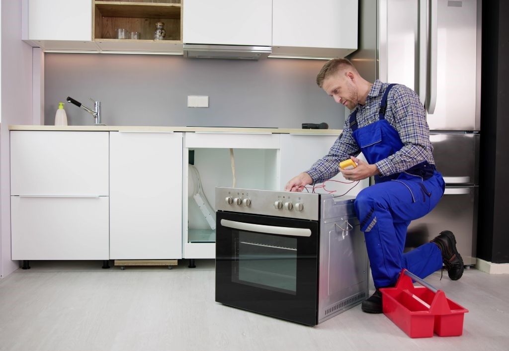 A man is fixing an oven in a kitchen.