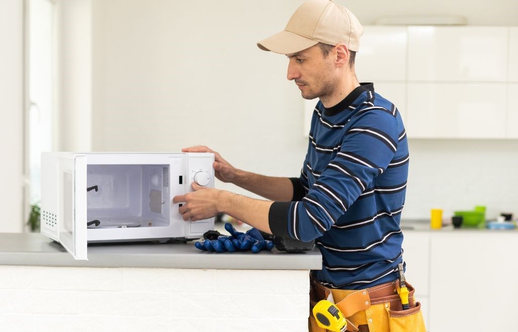 A man is fixing a microwave in a kitchen.