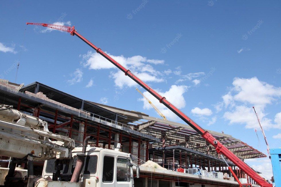 A red crane is sitting in front of a building under construction.