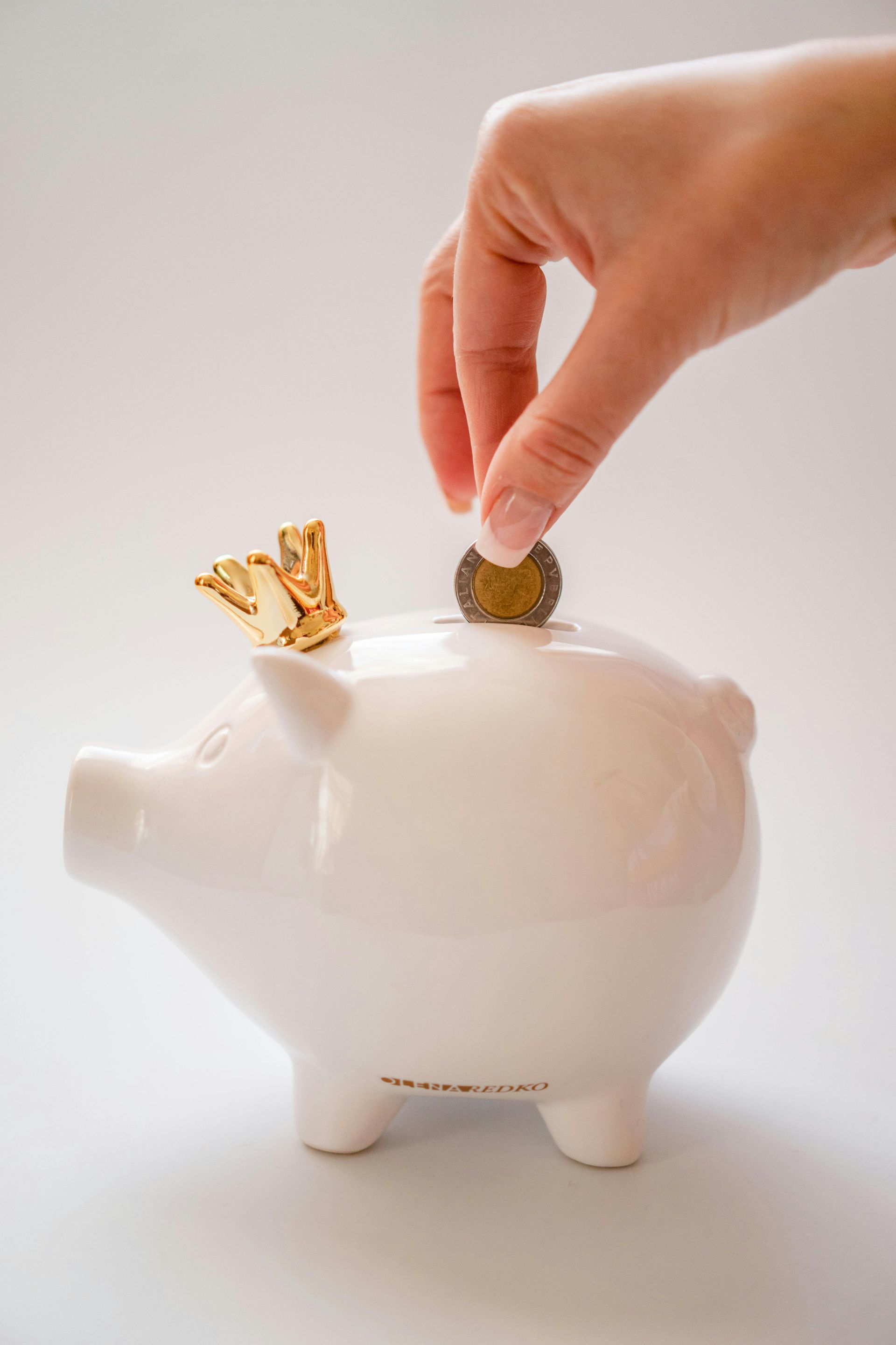 A person is putting a coin into a piggy bank with a crown on it.