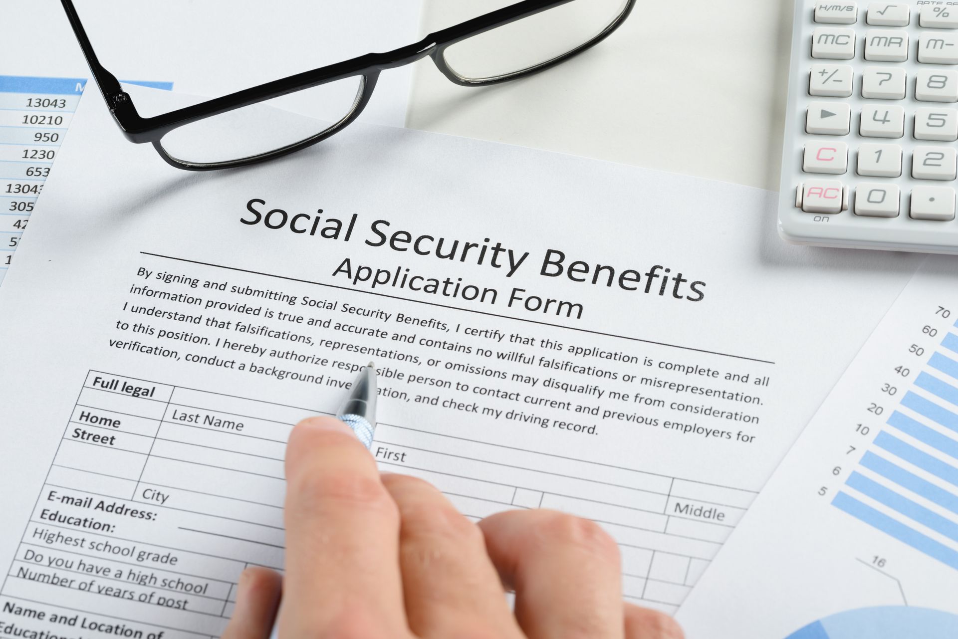 Social Security benefits application form with glasses, calculator, and hand filling it out