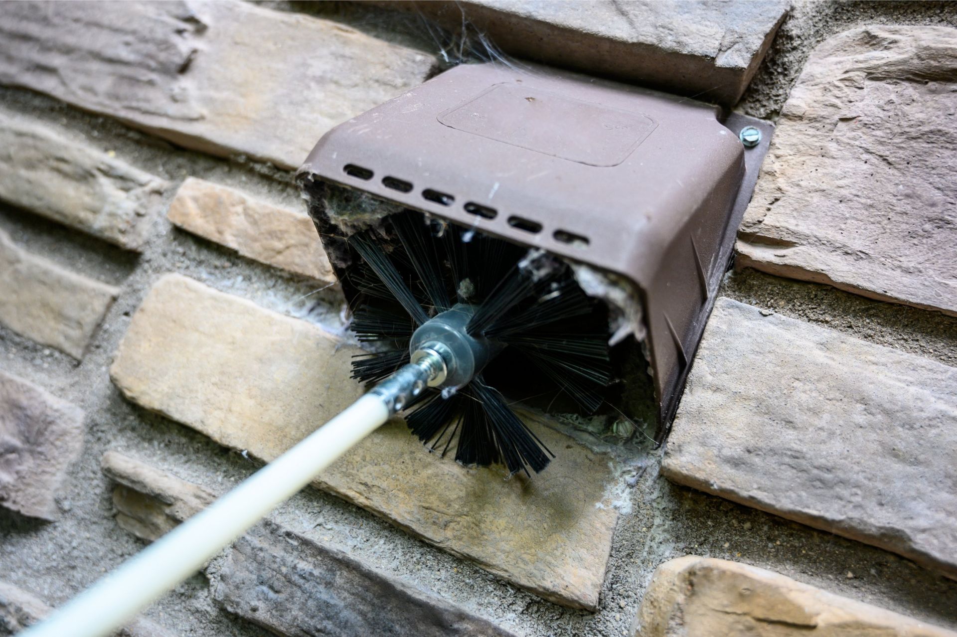 Cleaning a dryer vent with a brush on a wall made of stone bricks.