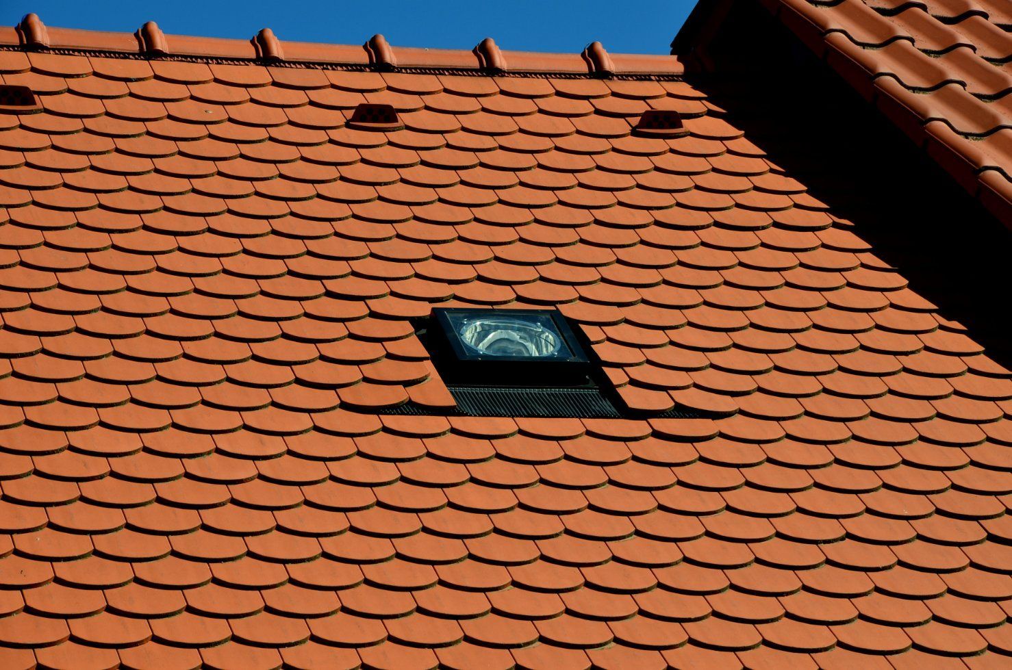 Red tiled roof with a skylight and small vent openings.