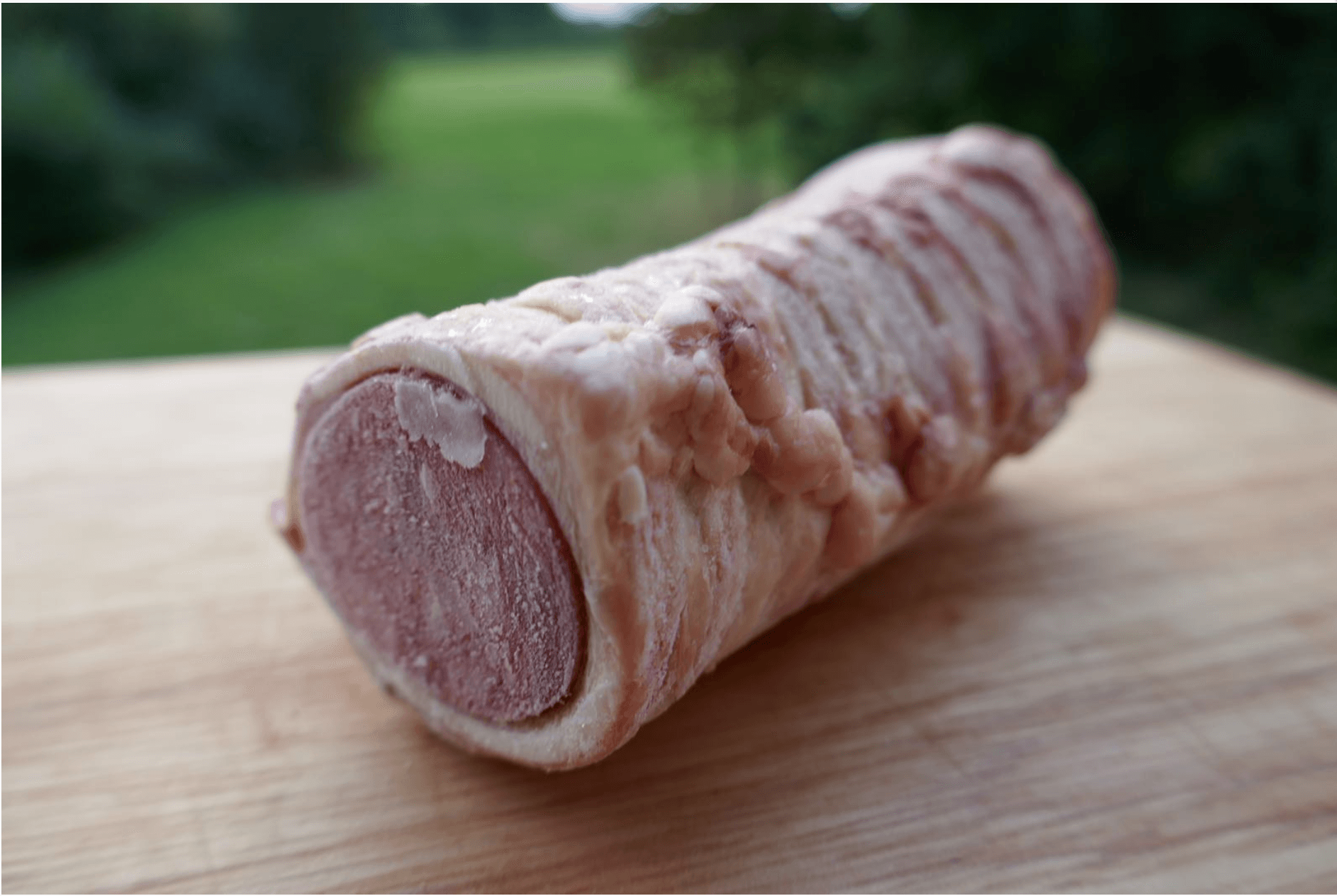 A piece of meat wrapped in bacon is sitting on a wooden cutting board.