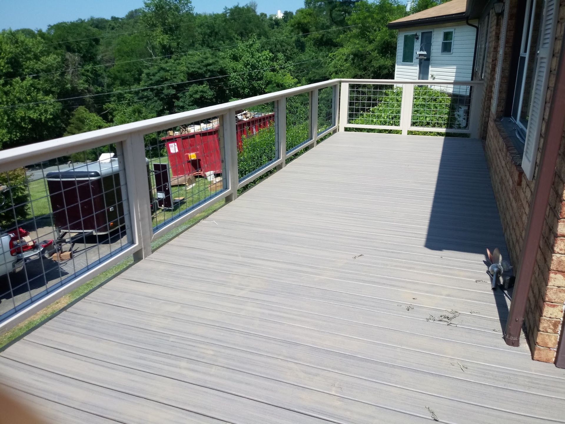 Deck with gray composite flooring, white railing, and metal wire detailing, adjacent to a brick house.
