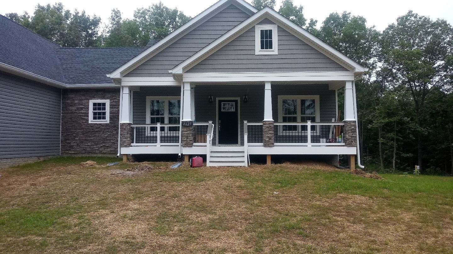 Gray house with porch, white columns, stone accents, and dark roof on grassy lot.