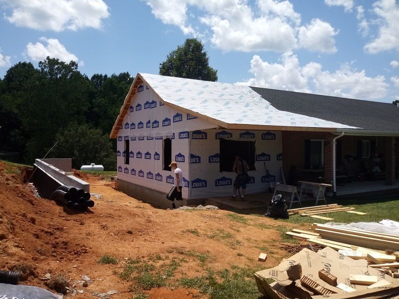 Construction site: a house addition with blue wrap, unfinished roof, workers.