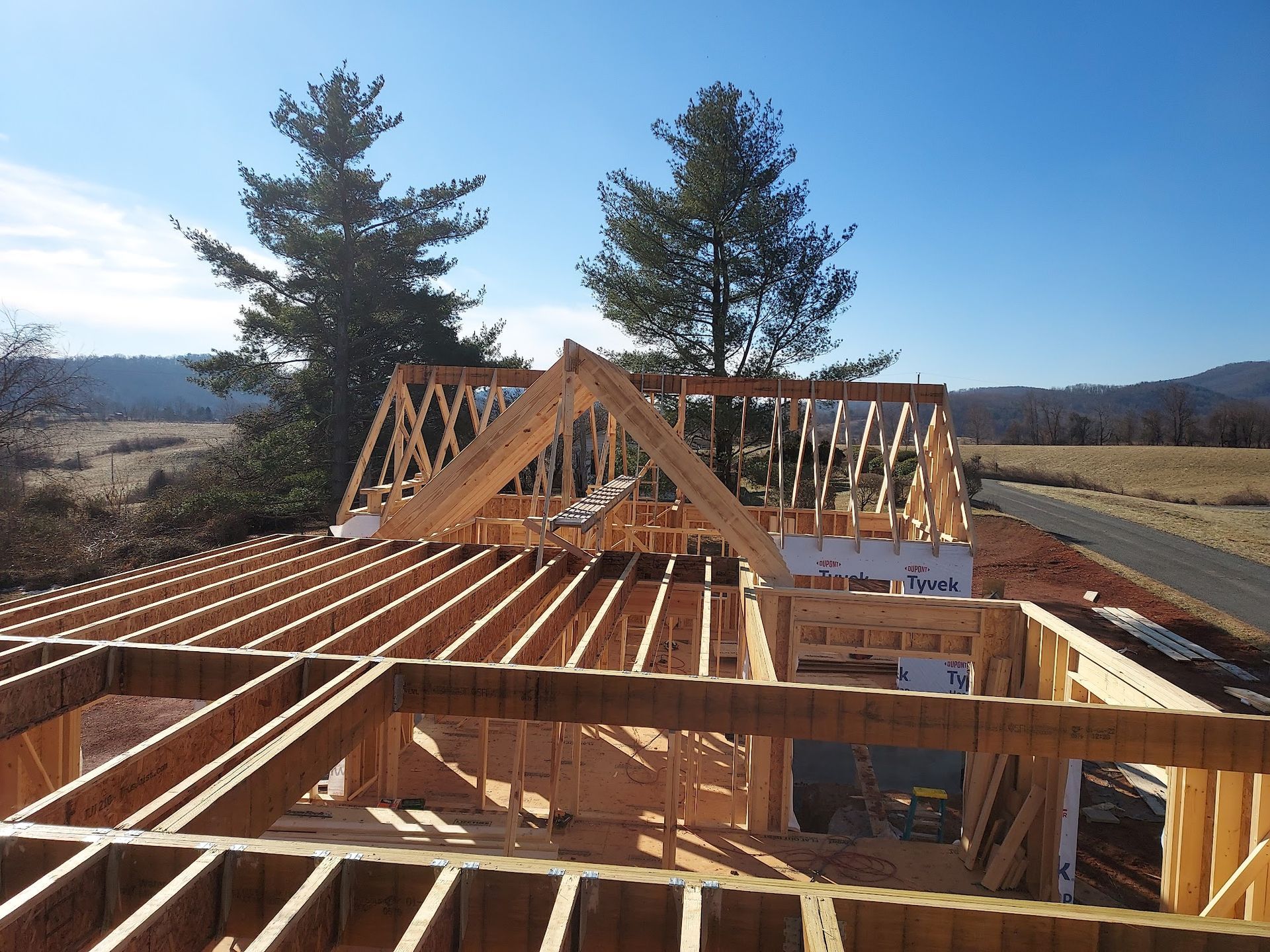 Framing of a house under construction with a gable roof, wood beams, and blue sky.