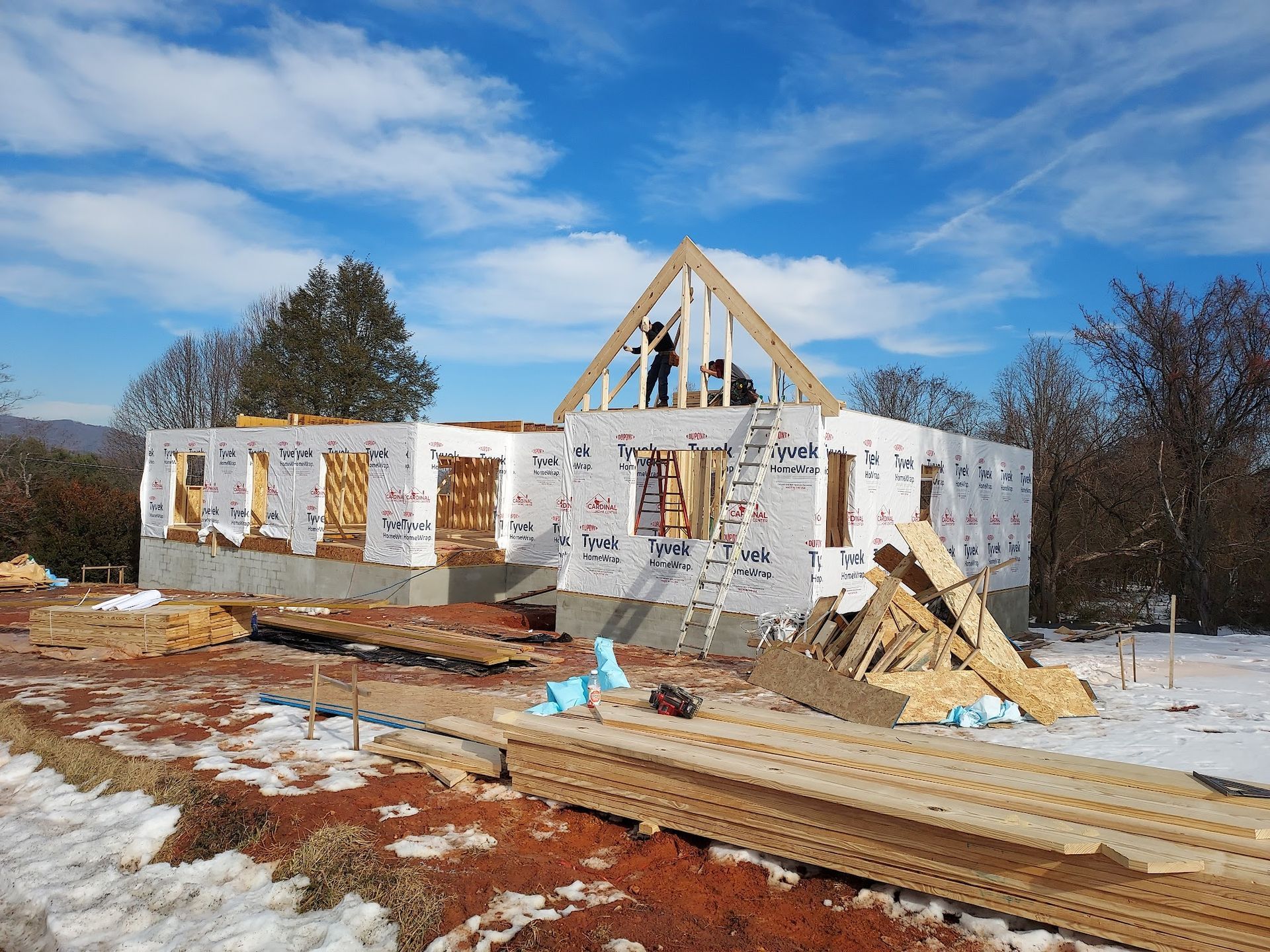 House under construction on a snowy day, a worker is on the roof frame, blue sky.