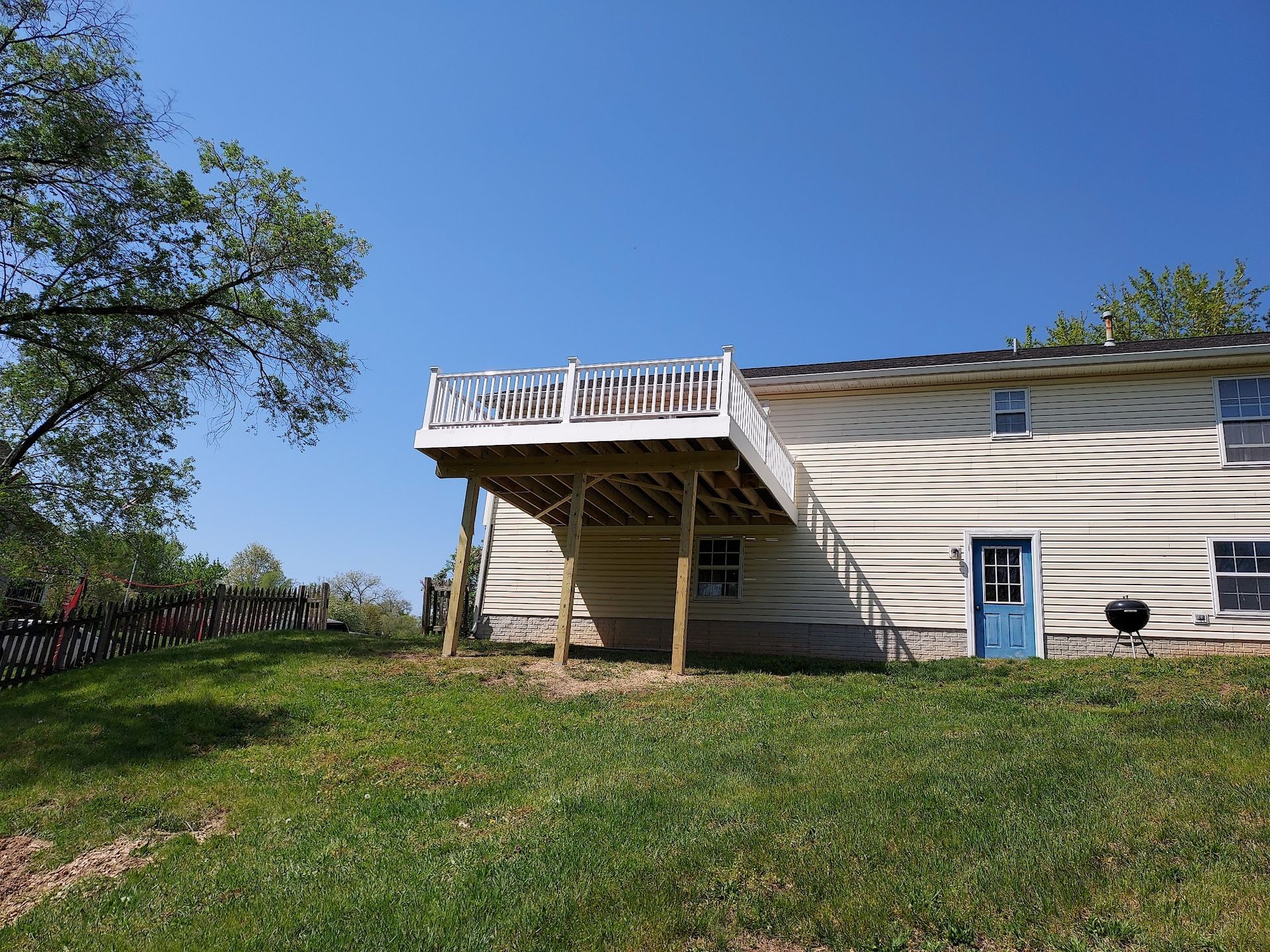 A wooden deck attached to a house with a blue door, supported by wooden posts, with a grassy yard.