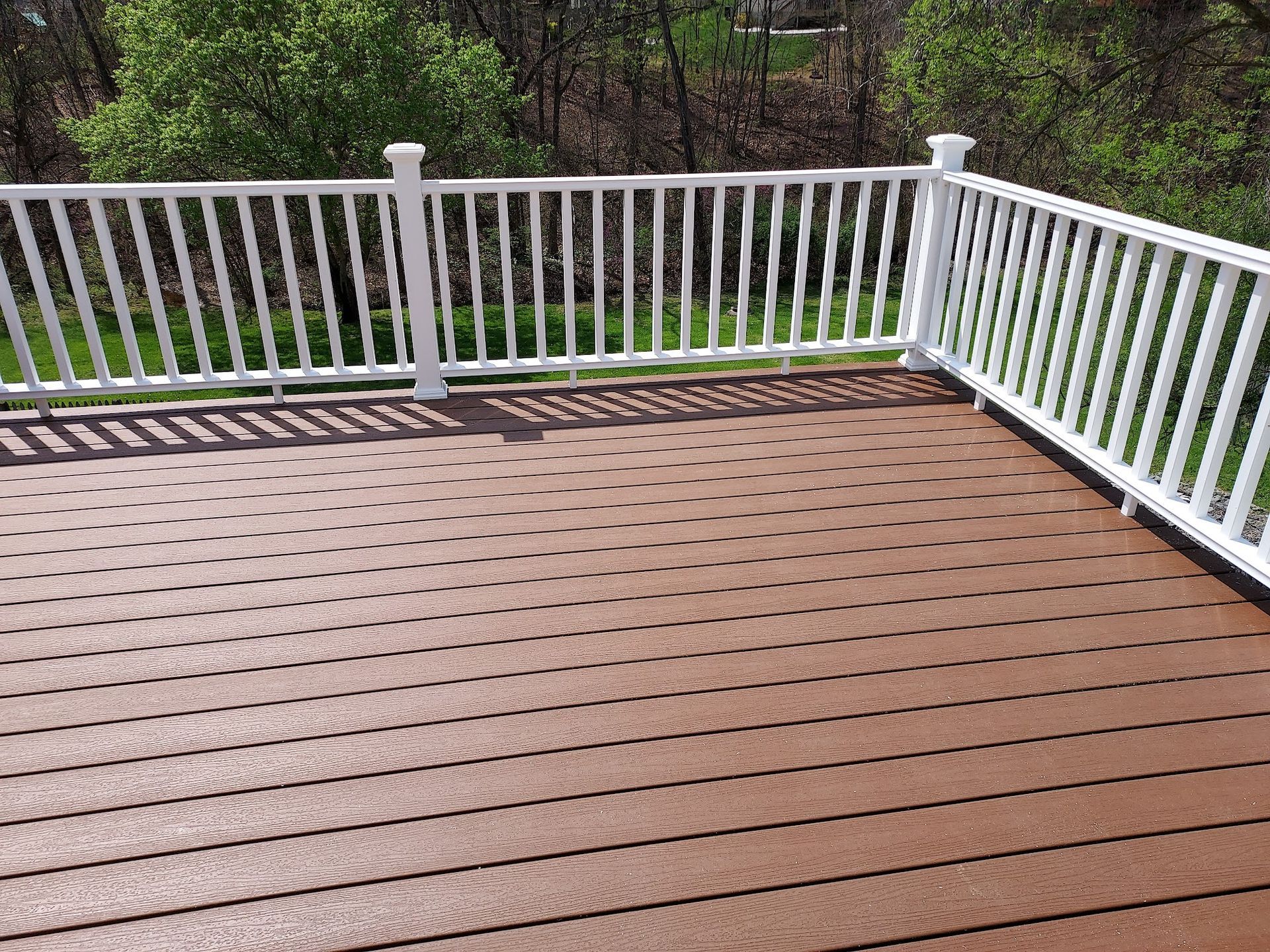 Brown composite deck with white railing, overlooking a green yard.