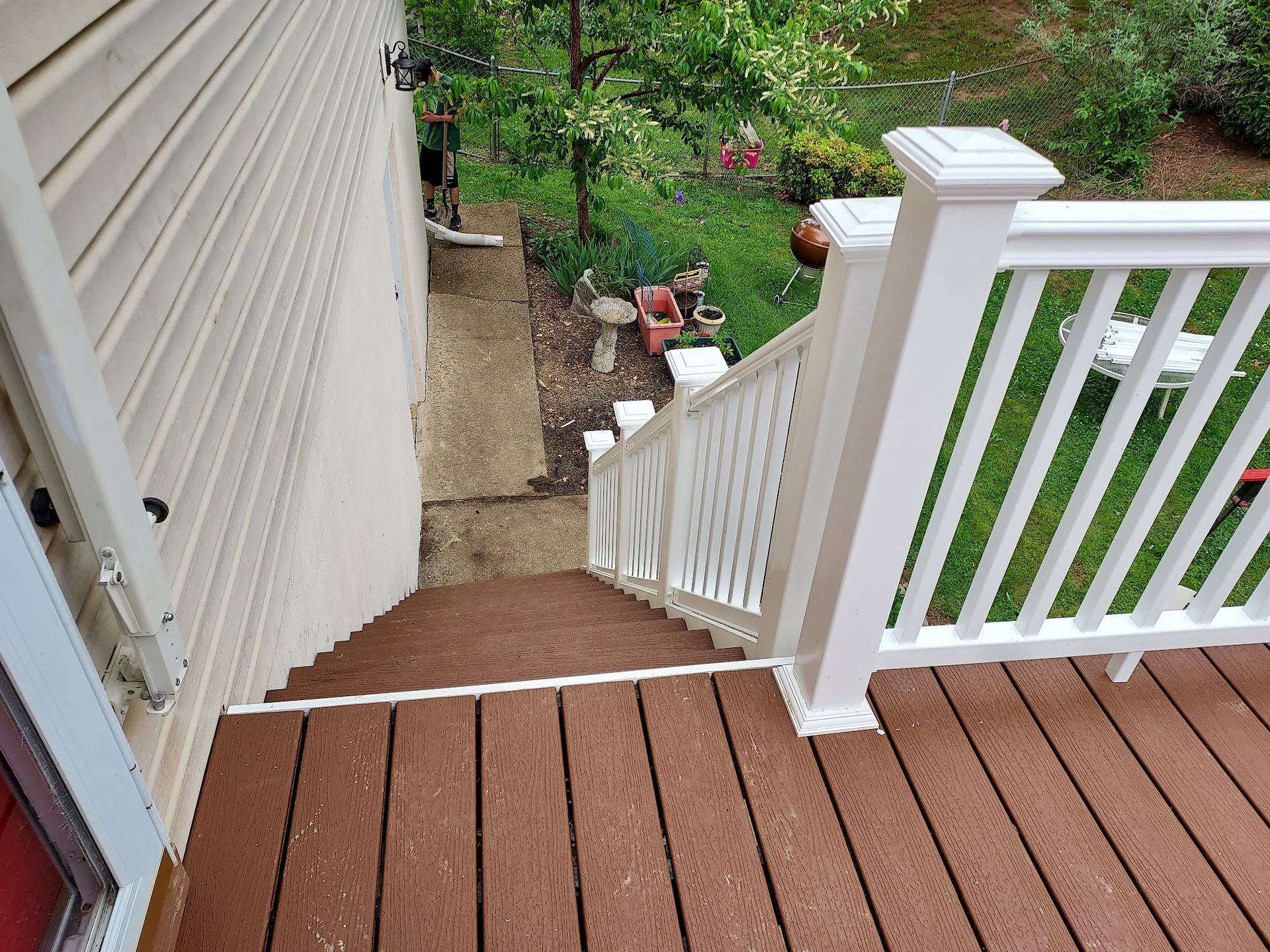 Brown deck leads to concrete steps and a garden, white railing.