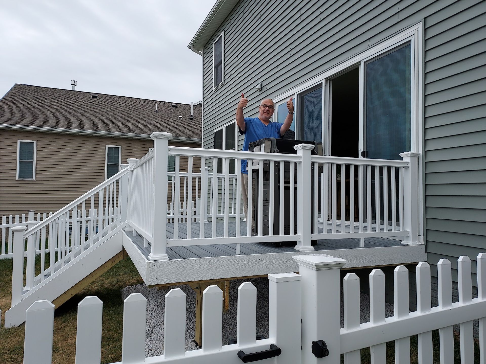 Man on white deck outside a two-story house, raising hands in front of open sliding doors.