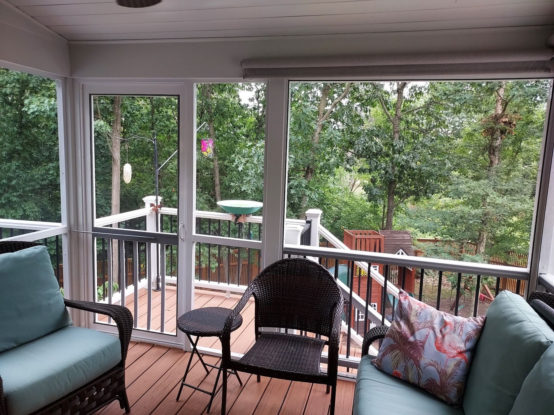 Screened porch overlooking a wooded backyard with outdoor furniture and a bird feeder.