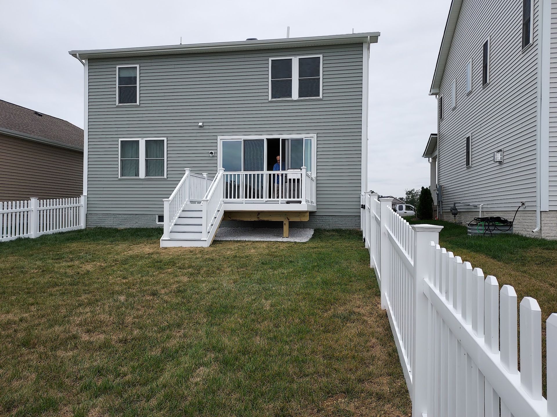 Backyard of a two-story house with a white picket fence, green grass, and a deck with sliding doors.