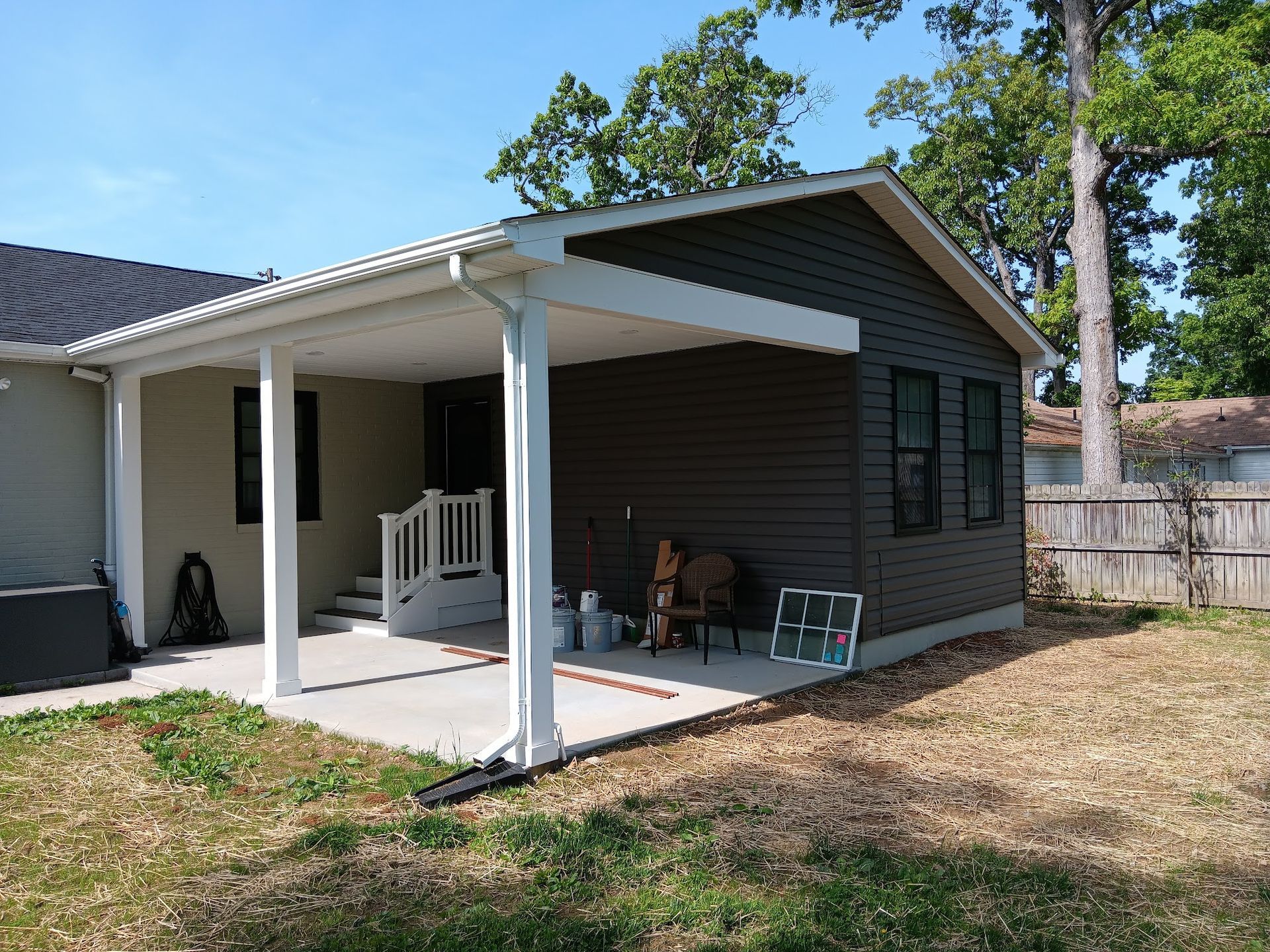 Exterior of a house with a covered patio. Gray and beige siding, white columns, and a concrete patio.
