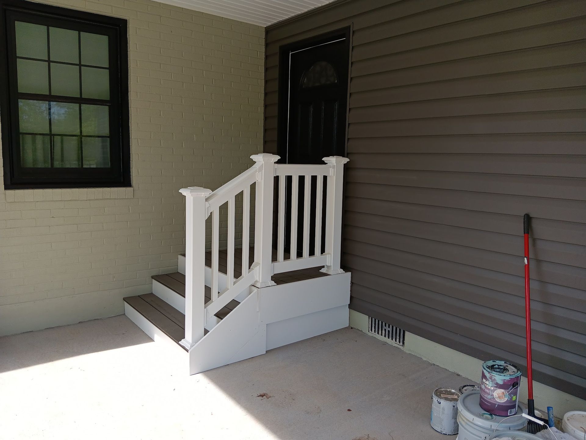 Steps with a white railing leading to a dark door, next to a window. The walls are a light brown and grey.