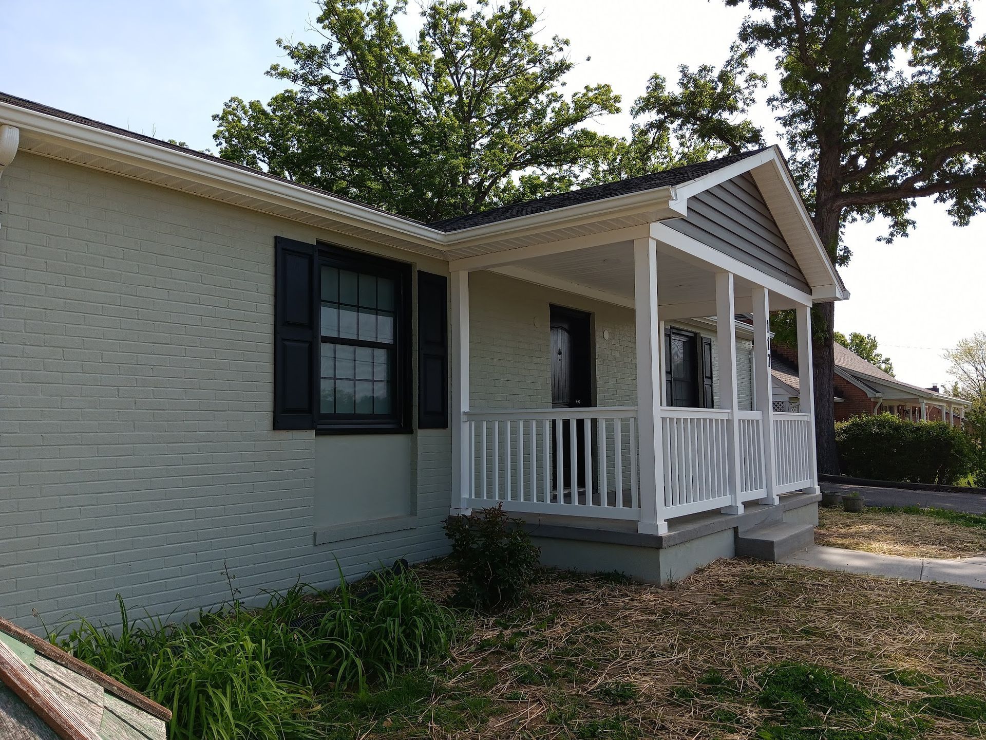 A light green brick house with a white porch and black shutters.
