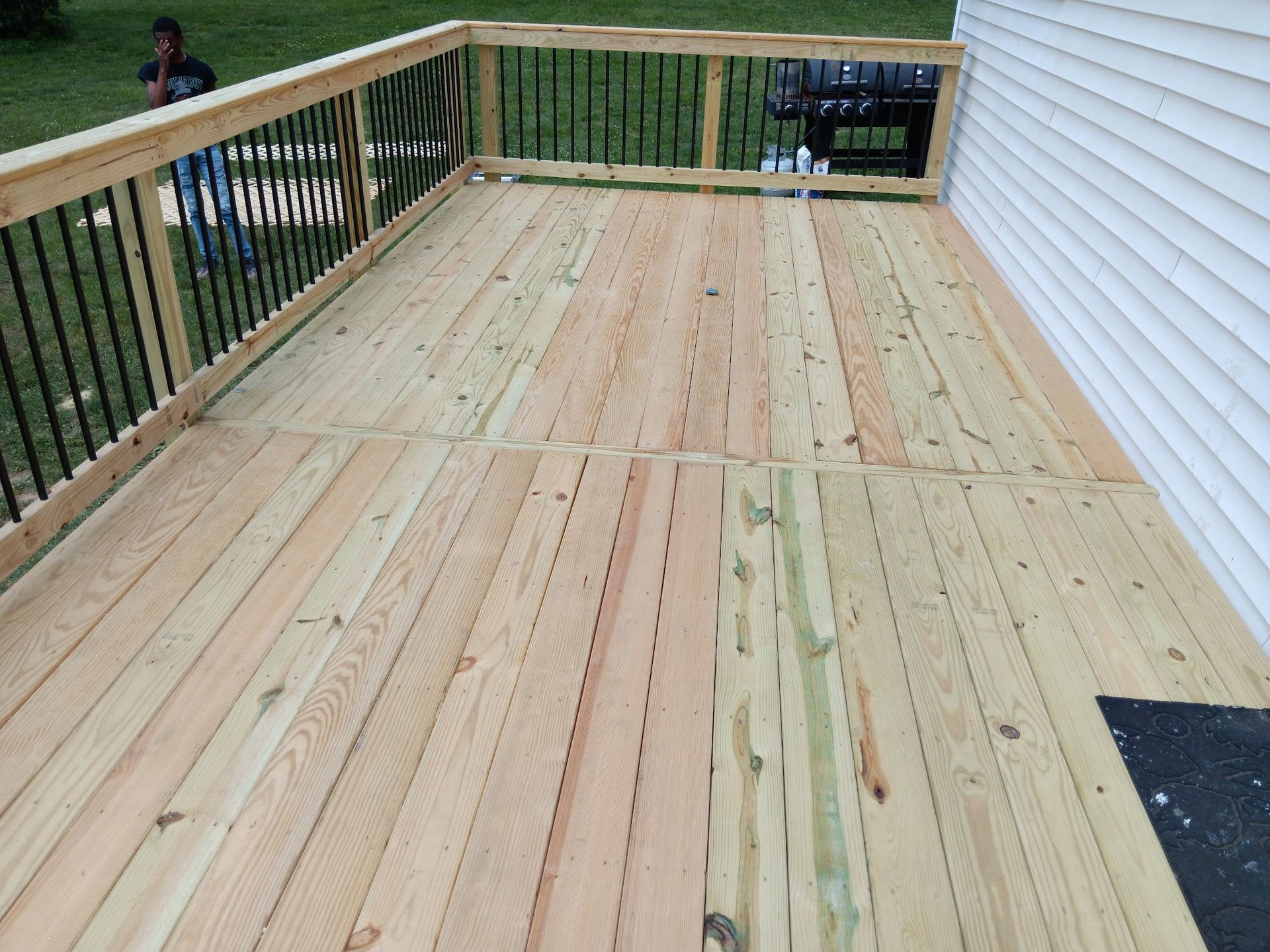 Wooden deck with black railing and grill next to a white house.