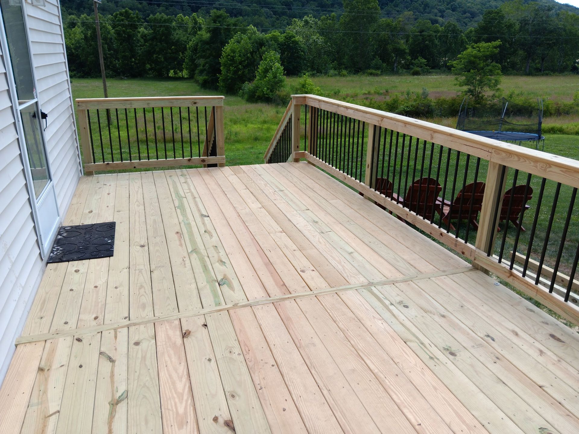 Wooden deck with black railing and grassy field in the background.