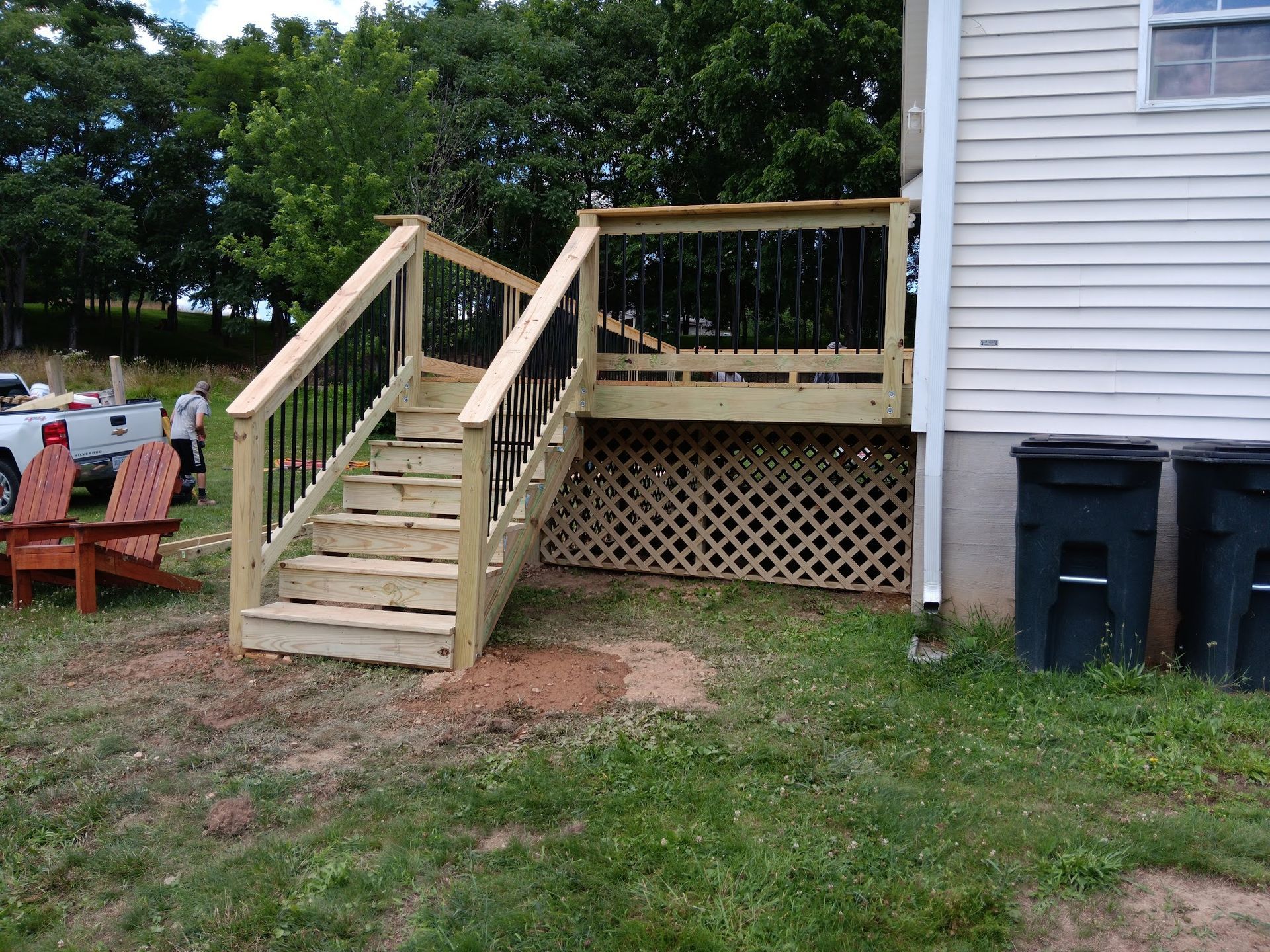 Wooden deck with stairs attached to a white house, black railing, lattice work below.