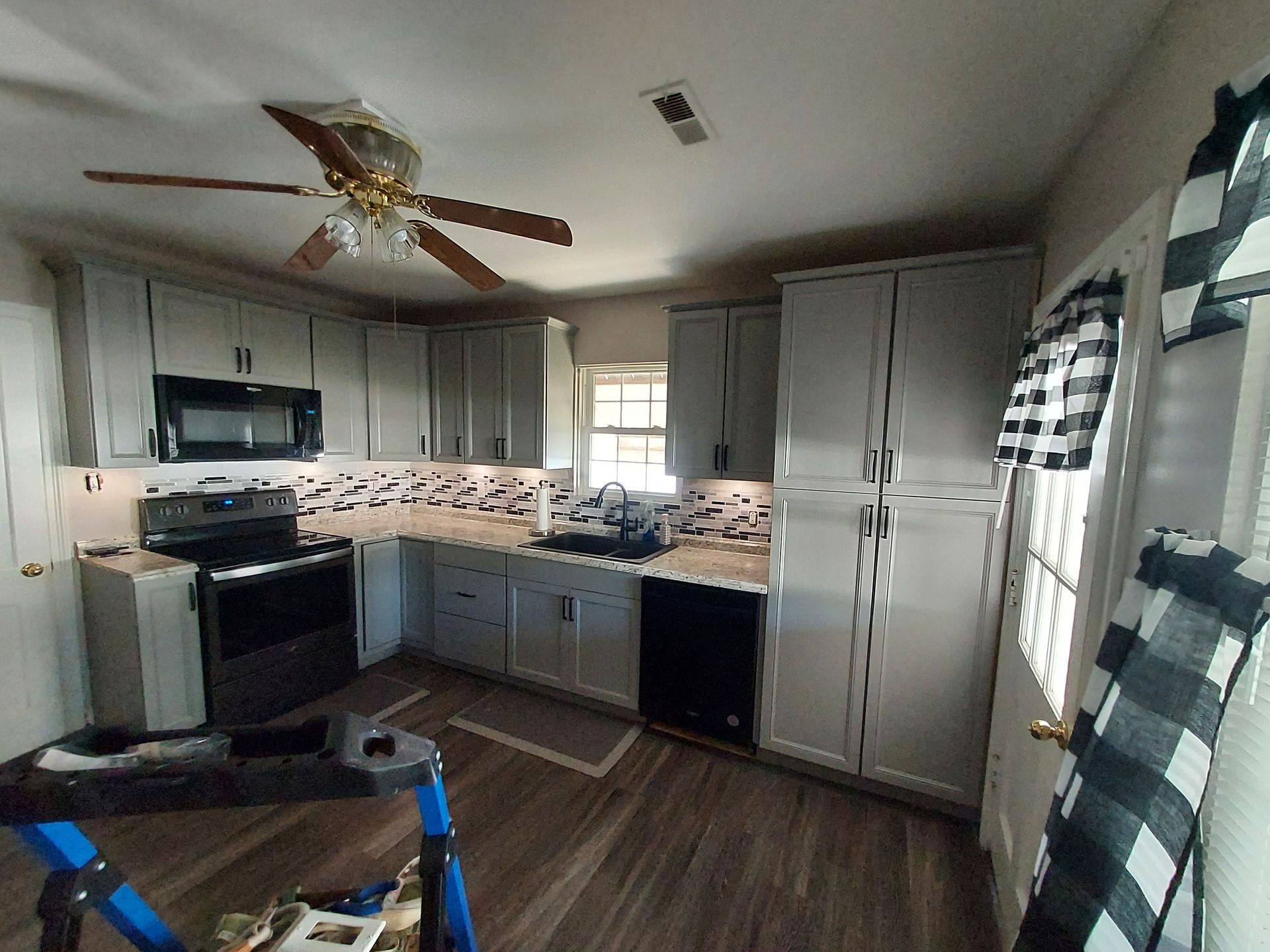 Two-story house under construction in a snowy forest. Unfinished exterior with wooden framing, windows, and a small deck.