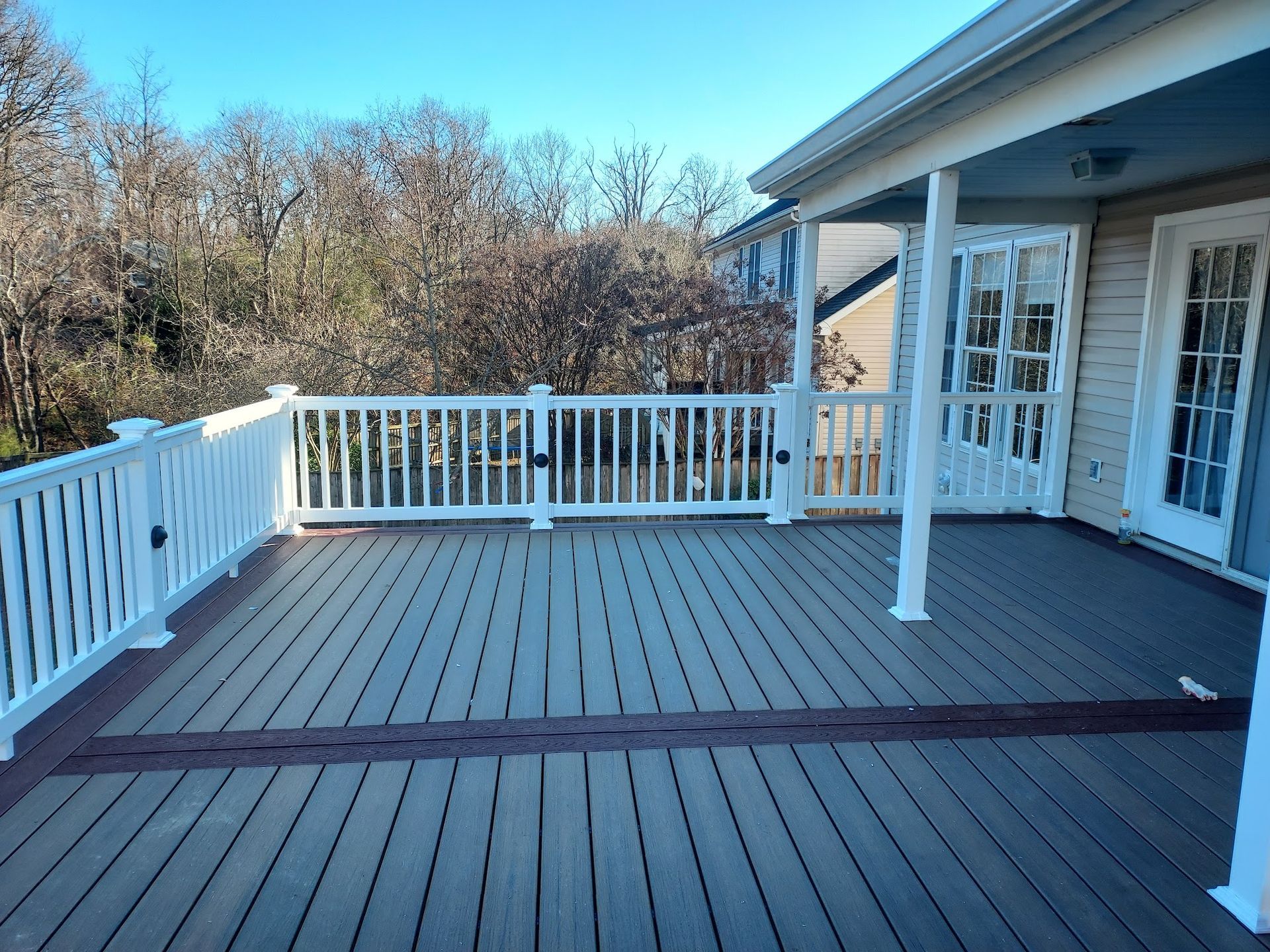 Wooden deck with white railing next to house. Overlooking trees under a blue sky.