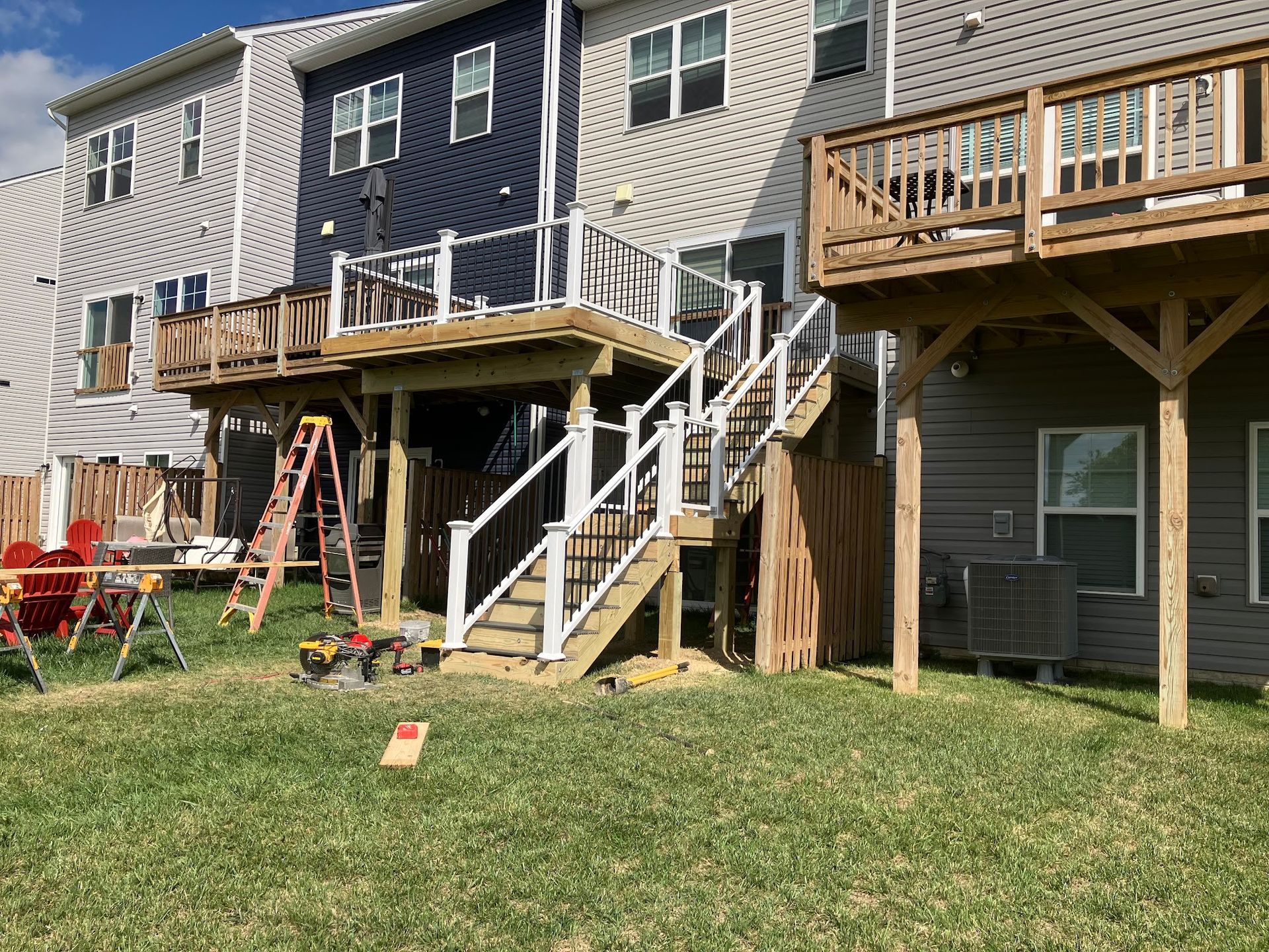 Backyard view of three connected houses with decks under construction. Construction materials and tools visible.