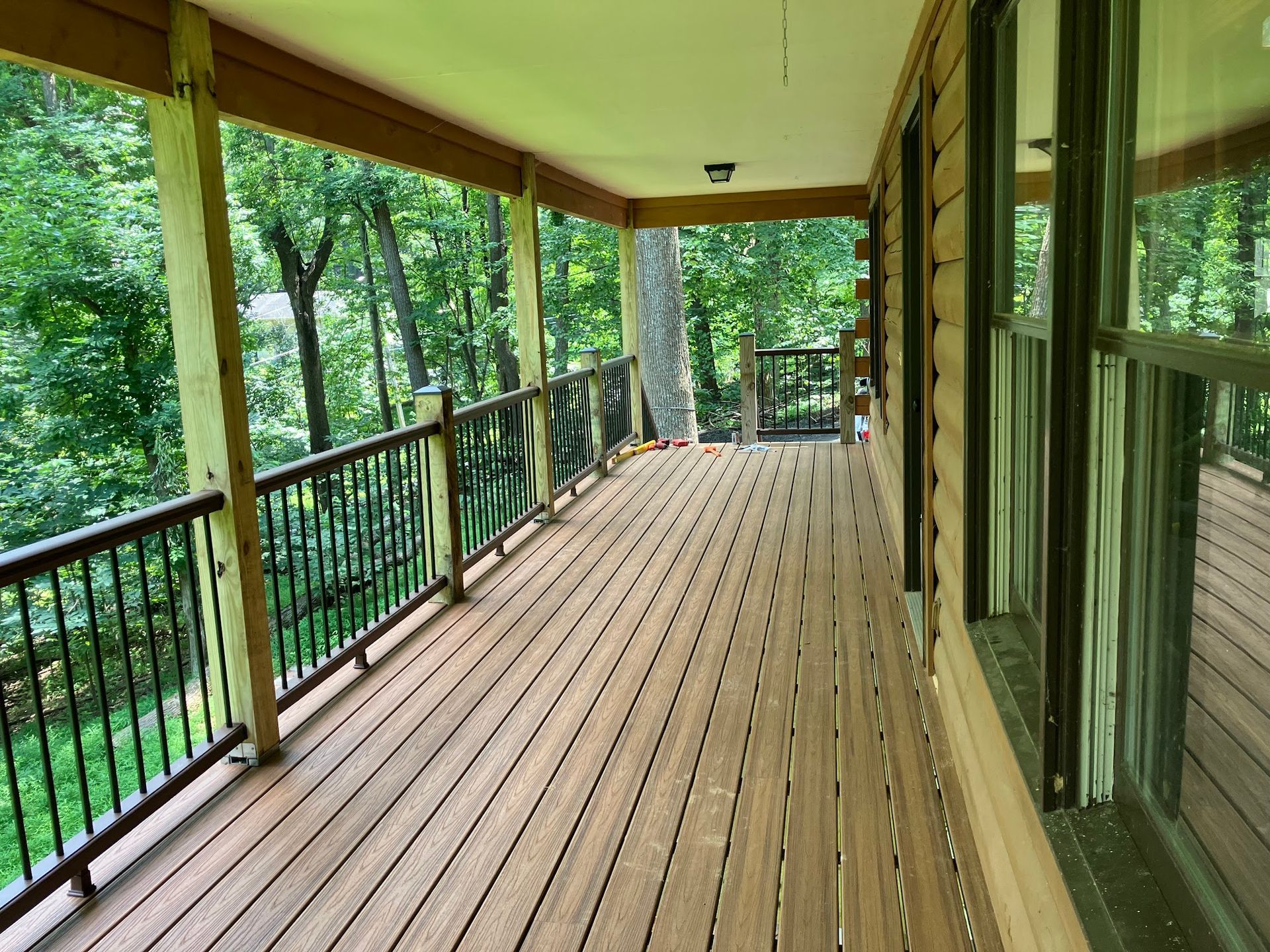 Wooden deck with dark railing, overlooking a green forest. Building has large windows.