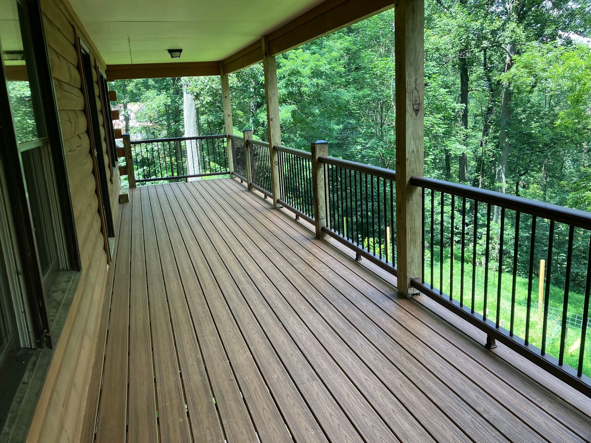 Covered wooden deck with black railing overlooking trees.