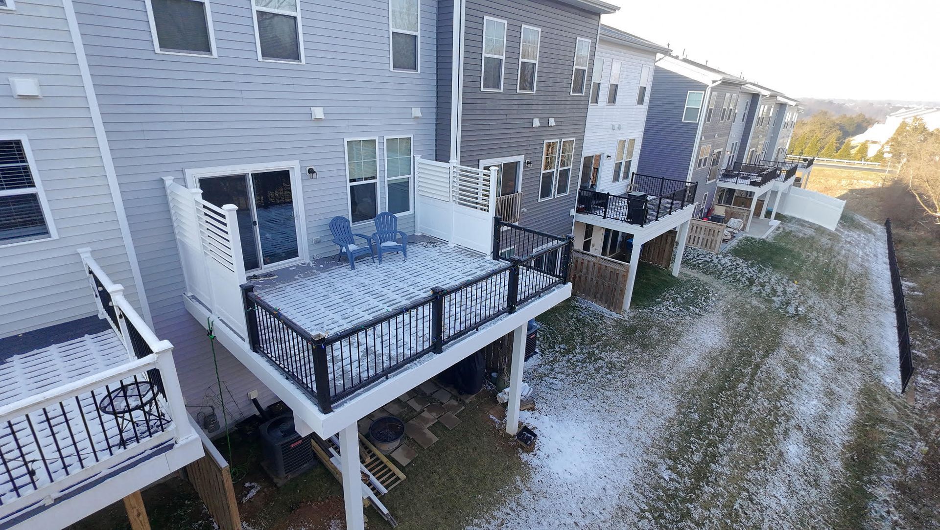 Row of townhouses with snow-covered decks and yards on a sunny day.