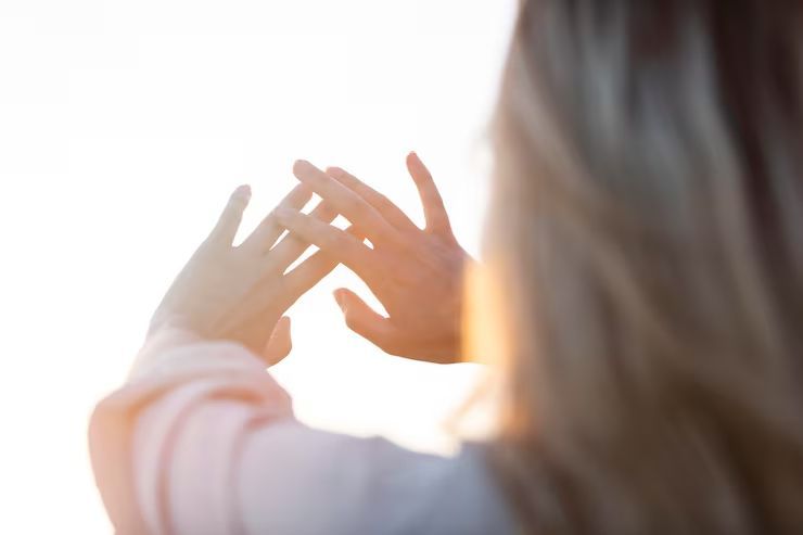 Hands raised toward bright sunlight, with a blurred person in the foreground