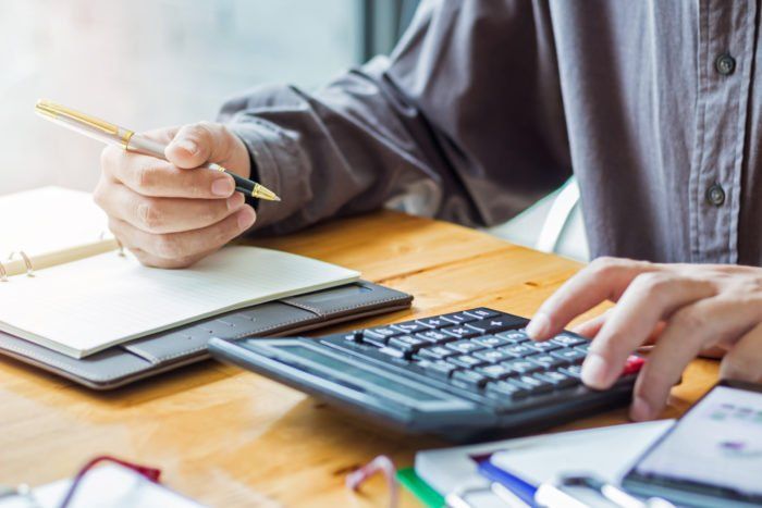 Person holding pen and looking at calculator